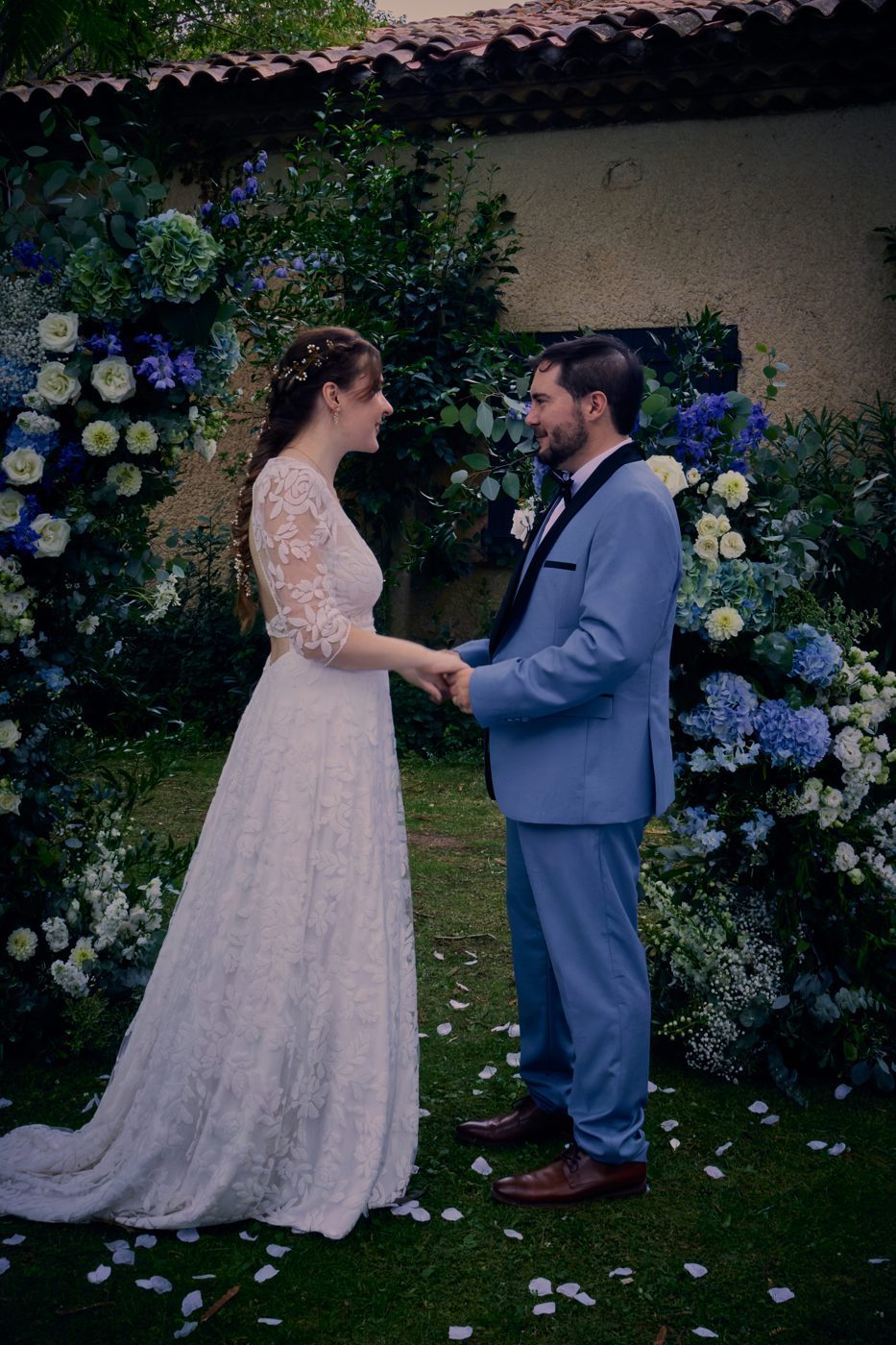 Les mariés se tenant les mains devant une arche de fleurs bleues